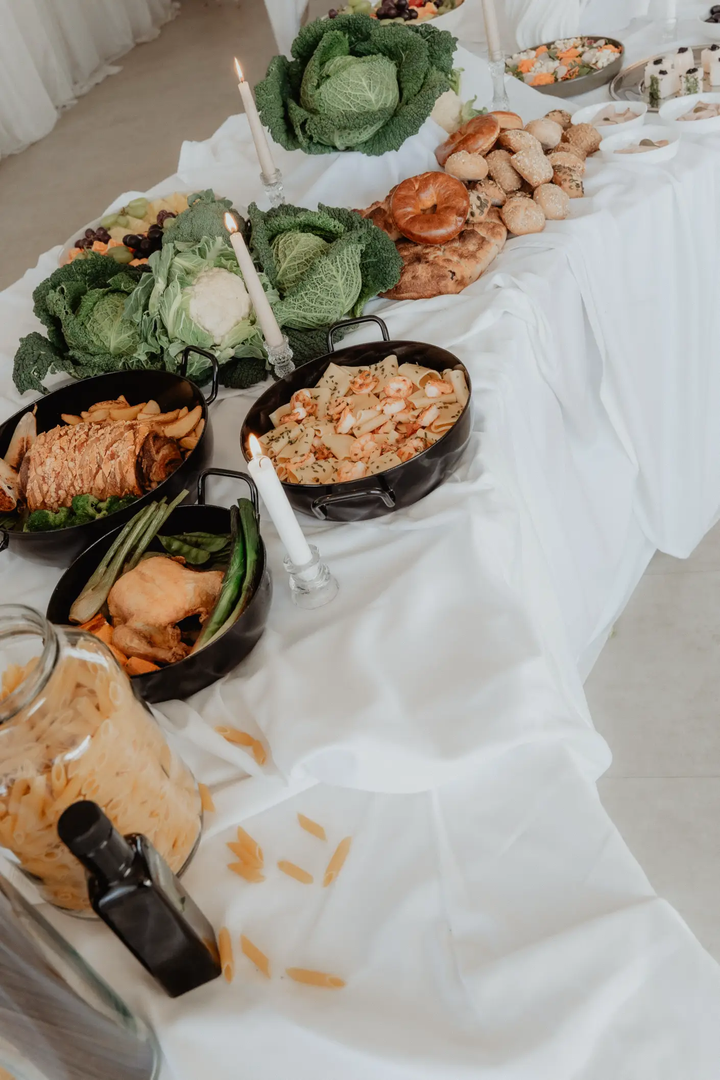 Na slici je prikazan svečano aranžiran buffet stol prekriven bijelim stolnjakom. Na stolu se nalaze ukrasne glavice kelja i cvjetače, košarica s različitim vrstama kruha i peciva, svijeće u staklenim svijećnjacima te crne posude s pripremljenom hranom